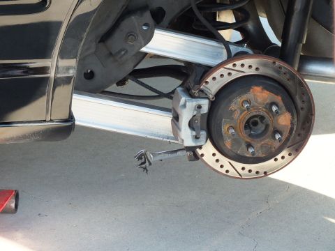 2003 Ford Crown Victoria - Exposed cross-drilled, slotted rotor with surface-rusted hat and gray caliper after wheel removal