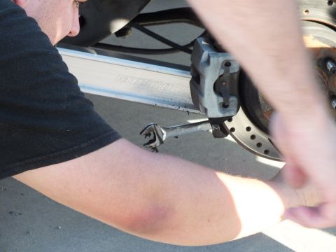 2003 Ford Crown Victoria - arm reaches under a vehicle to work a wrench on the caliper beside a cross-drilled rotor