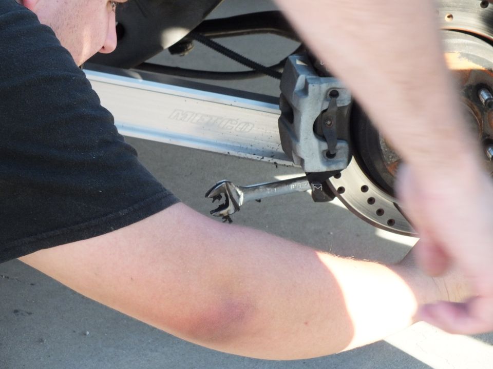 Person in black shirt using combination wrench on caliper near drilled brake rotor