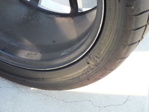 2003 Ford Crown Victoria - Detail of a black painted wheel spoke meeting the tire sidewall on a cracked concrete surface