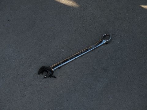 2003 Ford Crown Victoria - single chrome combination wrench rests on textured asphalt in raking sunlight