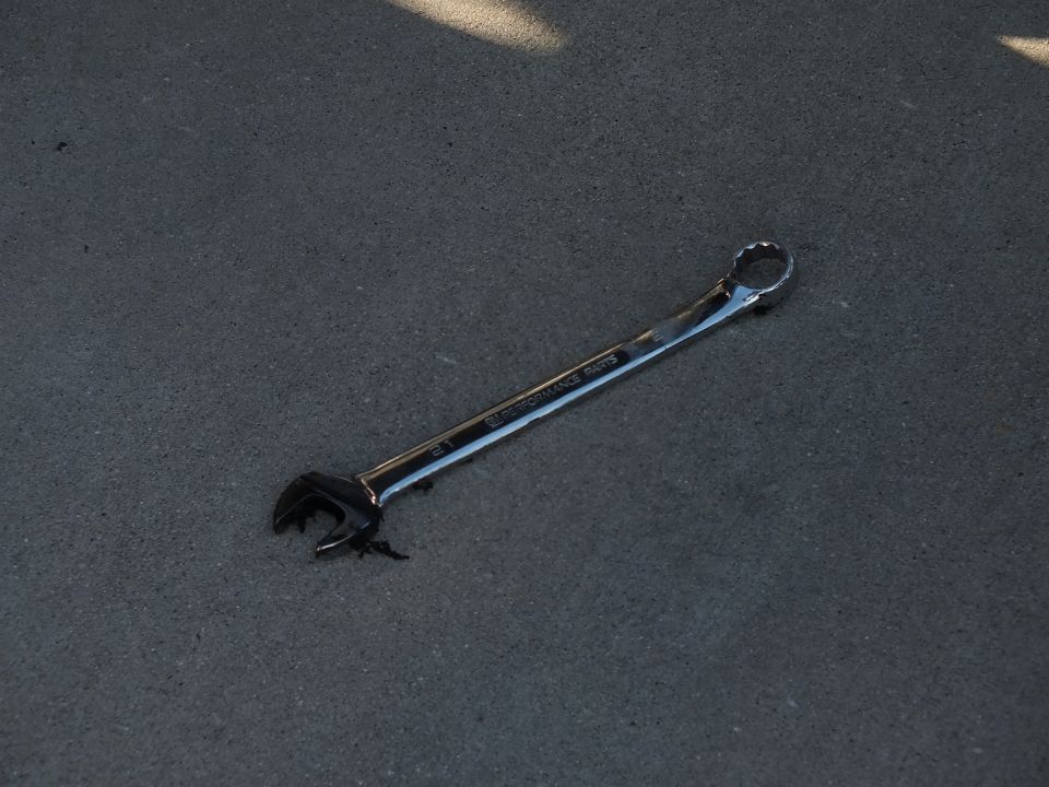 Chrome combination wrench lying on gray asphalt pavement