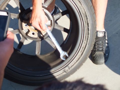 2003 Ford Crown Victoria - wrench works the lug area of a removed silver eight-spoke wheel laid flat on the concrete