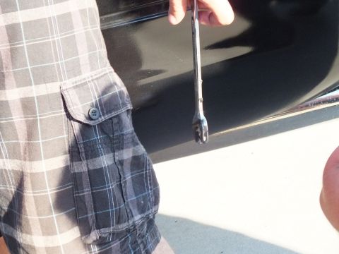 2003 Ford Crown Victoria - wrench is held flat against the glossy black side panel of a car next to a person in plaid shorts