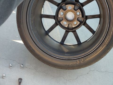 2003 Ford Crown Victoria - dismounted bronze-toned multi-spoke wheel rests on pavement with two lug nuts and a stud nearby