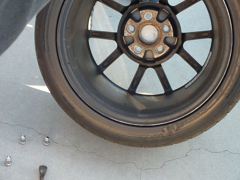 Removed bronze eight-spoke wheel on concrete with loose lug nuts beside it