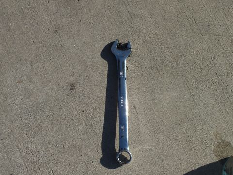 2003 Ford Crown Victoria - chrome combination wrench, its open jaw chewed up, lies on a concrete slab