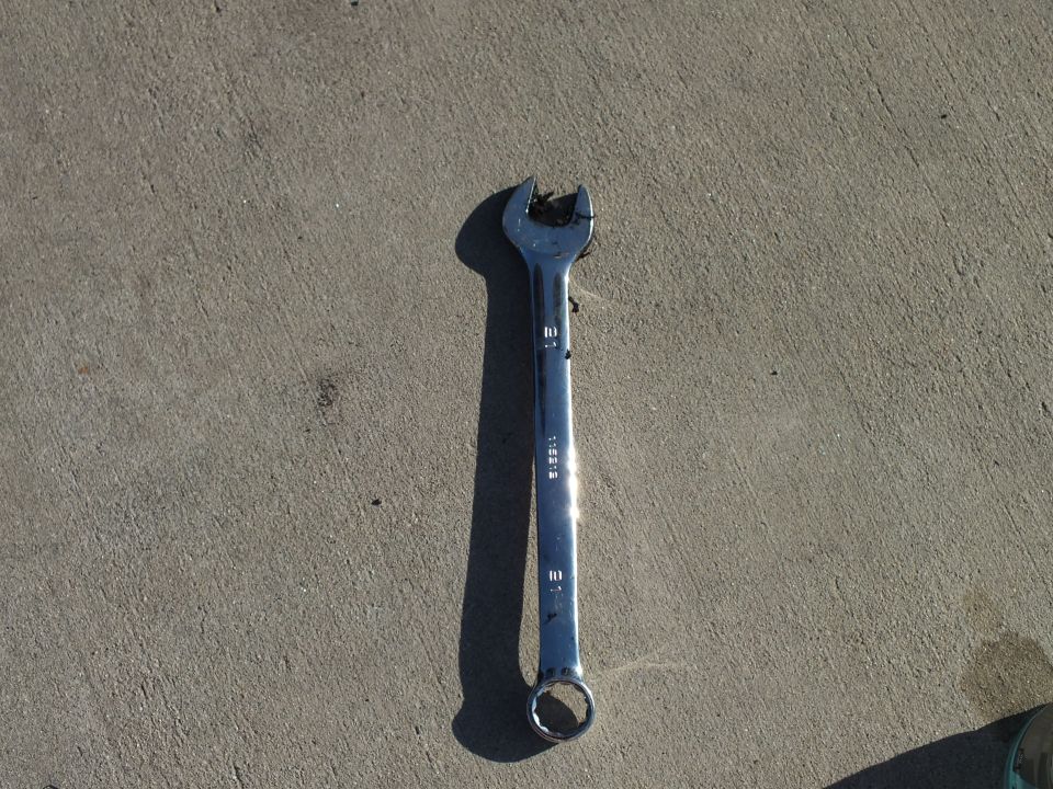 Chrome combination wrench with damaged open end on concrete surface