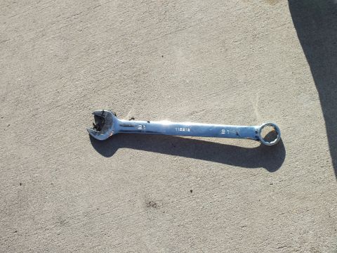 2003 Ford Crown Victoria - Combination wrench bearing the stamping 115212 rests on concrete, its open jaw deformed