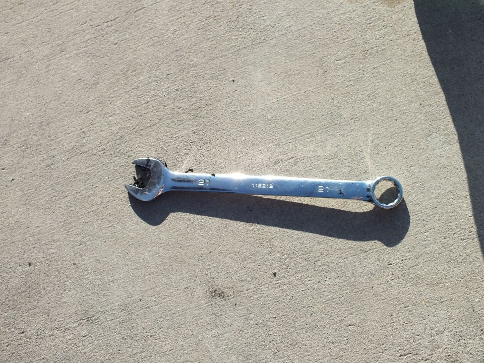 Chrome combination wrench stamped 115212 with worn open end on concrete