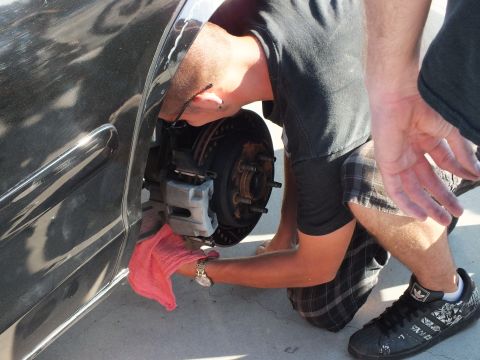 2003 Ford Crown Victoria - Kneeling at the wheel well of a black car, a person cleans the exposed brake hub with a red rag