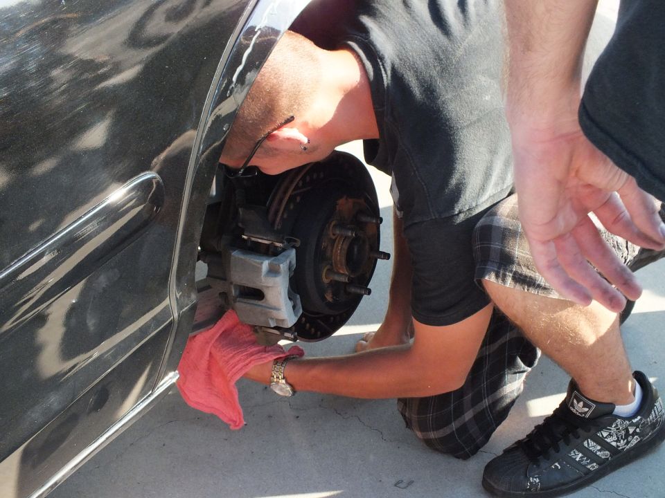 Person wiping bare brake hub and caliper with red rag on black car