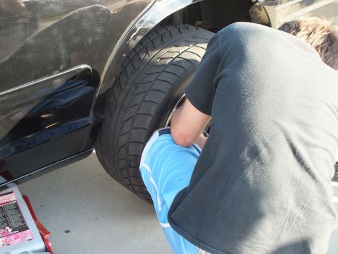 2003 Ford Crown Victoria - person bends into the rear wheel well of a black car next to the still-mounted tire