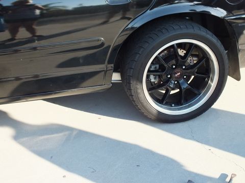 2003 Ford Crown Victoria - Rear three-quarter of a glossy black sedan riding on a black five-spoke wheel with polished lip