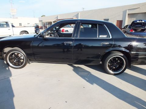 2003 Ford Crown Victoria - Side profile of a lowered black full-size sedan on black wheels parked outside an industrial building