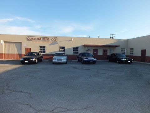 2003 Ford Crown Victoria - Frontal view of four full-size sedans parked before the tan Custom Mfg. Co. building