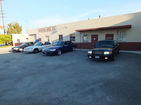 2003 Ford Crown Victoria - black sedan sits angled in the foreground lot near three other sedans by the Custom Mfg. Co. shop
