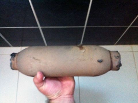 2001 Mercury Grand Marquis - A tan exhaust resonator with rust and black ends is held in a hand.