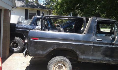 1979 Ford Bronco - Two Ford Broncos are parked side-by-side in a driveway, one appears to be undergoing modification.