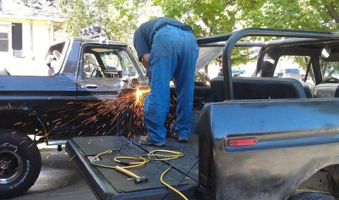 1979 Ford Bronco - A man welds a black Ford Bronco, with another Bronco visible in the background.