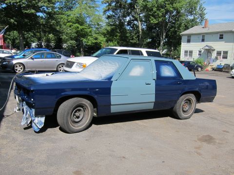 1991 Ford LTD Crown Victoria - A dark blue sedan is undergoing a paint job, with parts of the body covered in masking material and spray paint.