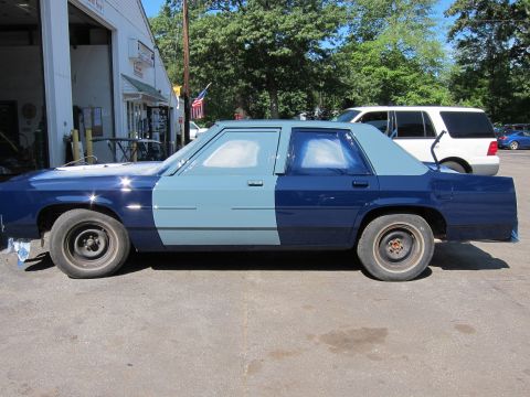 1991 Ford LTD Crown Victoria - A sedan is being painted in a two-tone blue scheme, with one side lighter than the other. A white SUV is visible in the background.