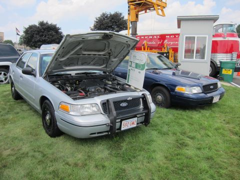 1991 Ford LTD Crown Victoria - silver Ford Crown Victoria police interceptor with its hood open sits beside a dark Crown Victoria cruiser on grass at a show.