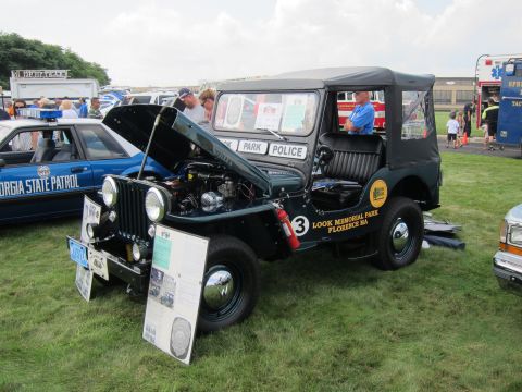 1991 Ford LTD Crown Victoria - dark-green soft-top 'Park Police' Jeep with its hood open and an information placard displayed at an outdoor vehicle show.