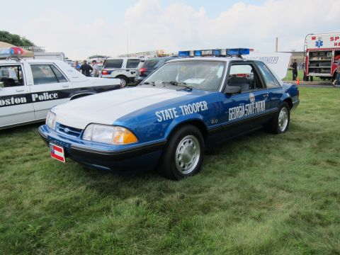 1991 Ford LTD Crown Victoria - blue-and-white Ford Mustang 5.0 marked 'Georgia State Patrol State Trooper' parked on grass at an outdoor vehicle show.