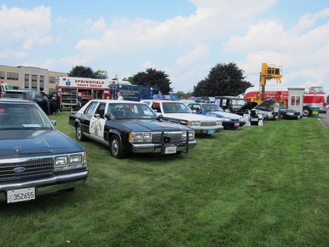 1991 Ford LTD Crown Victoria - line of vintage police cars, a sedan and a Springfield Heavy Rescue truck are parked across a grassy show field.