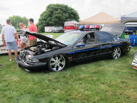 1991 Ford LTD Crown Victoria - lowered black Chevrolet Caprice with open hood, chrome wheels and a roof light bar draws onlookers at a car show.