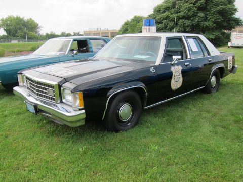 1991 Ford LTD Crown Victoria - black-over-white Ford police sedan marked 45 with a chrome badge emblem and blue roof light sits on grass.