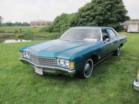 1991 Ford LTD Crown Victoria - teal-green full-size Chevrolet four-door sedan with chrome grille and red plate sits on grass near a pond.