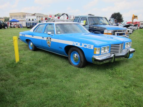 1991 Ford LTD Crown Victoria - light-blue Pontiac police sedan lettered POLICE with a roof light bar and bumper push bar is shown on grass.