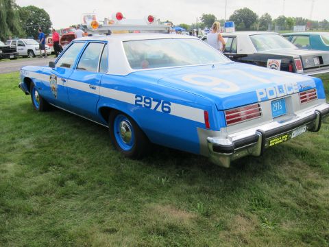 1991 Ford LTD Crown Victoria - Rear three-quarter view of a blue police sedan marked POLICE 2976 with roof lights, parked on a grassy field.
