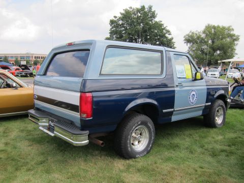 1991 Ford LTD Crown Victoria - two-tone blue Ford Bronco SUV with chrome bumper and round agency seal on the door sits rear-three-quarter on grass.