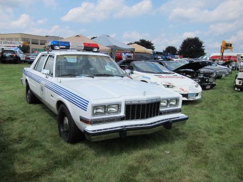 1991 Ford LTD Crown Victoria - white police sedan with blue side striping, a door seal and roof light bar is displayed on a grassy field.