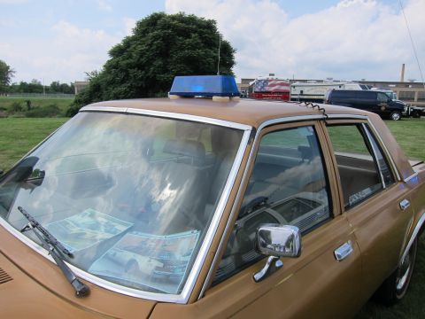 1991 Ford LTD Crown Victoria - Close-up of a gold police sedan's windshield and roof light, with display papers tucked on the dashboard.