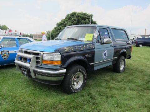 1991 Ford LTD Crown Victoria - two-tone blue Ford Bronco with painted lettering, push bar and door seal sits front-quarter on a grassy show field.