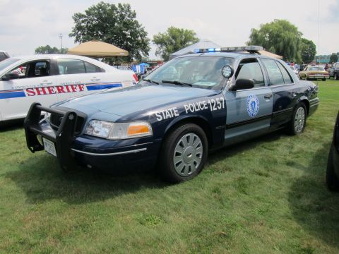 1991 Ford LTD Crown Victoria - dark blue Ford Crown Victoria marked State Police 1257 with a front push bar and roof lightbar sits on grass at a vehicle show.