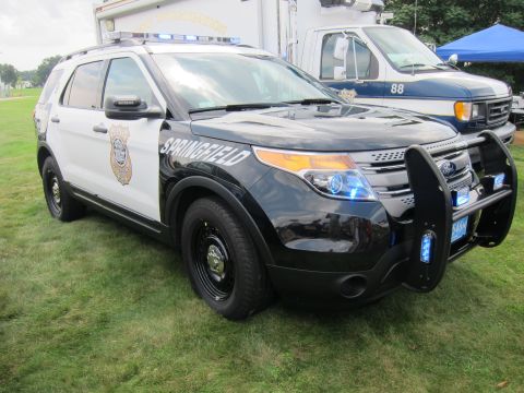 1991 Ford LTD Crown Victoria - black-and-white Ford Explorer marked Springfield with a front push bar and roof lightbar parked on grass beside other emergency vehicles.