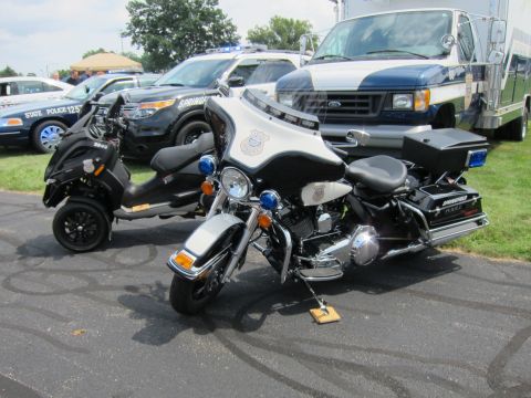 1991 Ford LTD Crown Victoria - black-and-white Harley-Davidson police motorcycle with hard cases stands on pavement in front of patrol SUVs and a command vehicle.