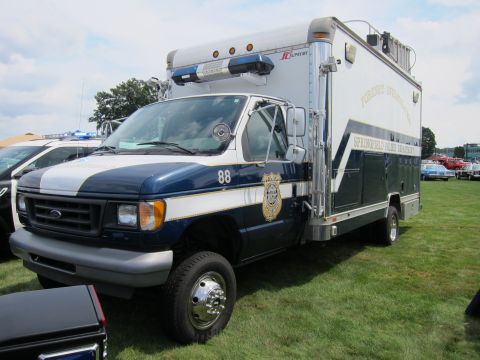 1991 Ford LTD Crown Victoria - blue-and-white Ford E-series cutaway box truck numbered 88, fitted with a roof lightbar, parked on grass as a police support vehicle.