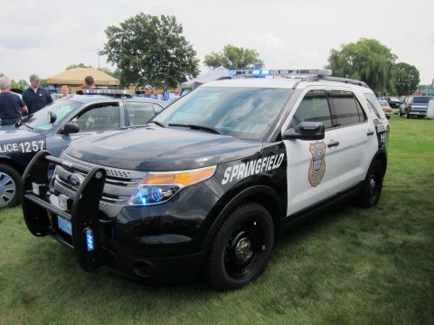1991 Ford LTD Crown Victoria - black-and-white Ford Explorer marked Springfield with a push bar and blue lights, parked on grass beside a Crown Victoria cruiser.