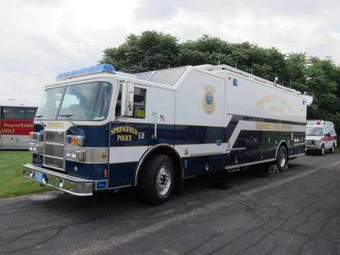1991 Ford LTD Crown Victoria - large blue-and-white truck lettered Springfield Police Mobile Command Center sits on pavement near an ambulance and other vehicles.