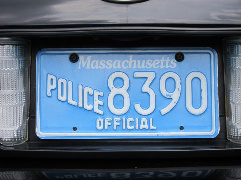 1991 Ford LTD Crown Victoria - blue Massachusetts plate reading POLICE 8390 OFFICIAL mounted on the rear of a dark-colored vehicle between taillights.