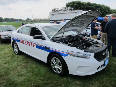 1991 Ford LTD Crown Victoria - white Ford Taurus Sheriff cruiser number 1 with red and blue striping and an open hood, parked on grass beside other police cars.