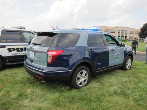 1991 Ford LTD Crown Victoria - rear quarter of a two-tone blue Ford Explorer State Police SUV with roof lights, parked on grass in front of a building.