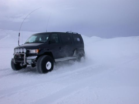 1996 Ford Bronco - A modified van navigates a snowy landscape with large tires kicking up snow.