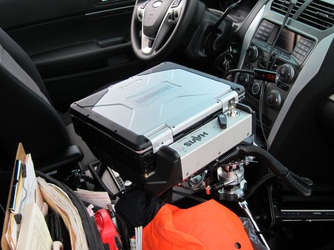 1991 Ford LTD Crown Victoria - police SUV interior showing a Ford wheel, a rugged laptop on a Havis mount, console radios, and an orange item on the seat.